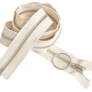 May include: A white zipper with a silver slider and pull tab. The zipper is made of a cotton tape and has a herringbone pattern.