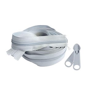May include: A roll of light gray zippers with two matching zipper pulls. The zippers are coiled, showing the teeth and tape. The zipper pulls have a ring at the end.