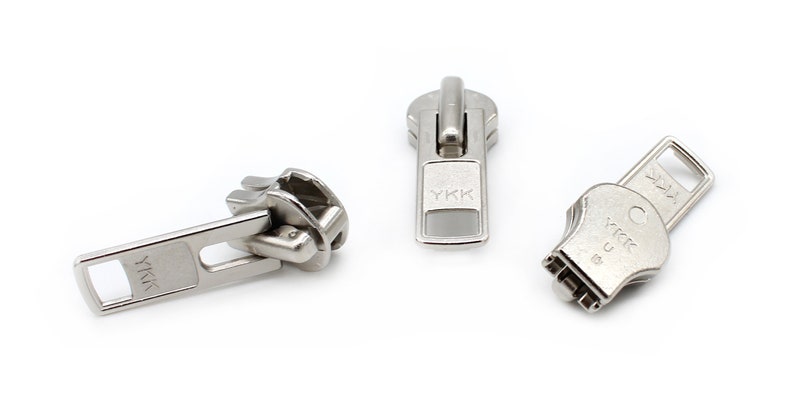May include: Three silver metal zipper pulls with the YKK logo. The zipper pulls are in different styles.