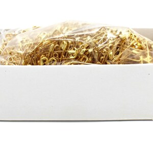 May include: A white box filled with a clear plastic bag of gold safety pins.