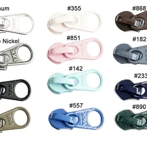 May include: Assortment of zipper pulls in various colors, including aluminum, antique nickel, white, pink, light blue, black, dark blue, and green. Each pull features the YKK logo and a unique number.