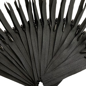 May include: A bulk pack of black zipper pulls. The zippers are arranged in a fan shape and are ready to be used for sewing projects.