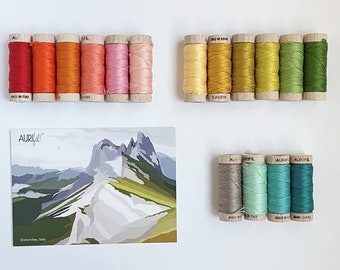 May include: A set of 10 spools of embroidery floss in various shades of orange, yellow, green, and blue. The floss is arranged in two rows, with a postcard featuring a mountain landscape in the center. The postcard reads "Dolomites, Italy".