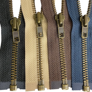 Puede incluir: Cinco cierres de cremallera con deslizadores y dientes de latón. Las cremalleras son de tela negra, beige, marrón y azul.