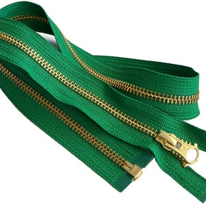 以下が含まれることがあります： 金色の金属製のジッパーのスライダーが付いた緑色のジッパー。ジッパーは閉まっており、スライダーはジッパーの中央にあります。