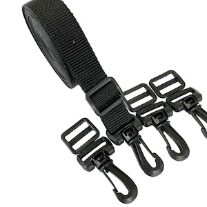 May include: Black nylon strap with three black plastic clips. The strap is rolled up and the clips are attached to the strap.