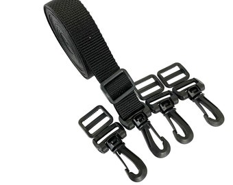 May include: Black nylon strap with three black plastic clips. The strap is rolled up and the clips are attached to the strap.