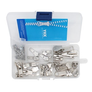 May include: A clear plastic storage box filled with silver zipper pulls. The box has a blue lid and a label that reads "YKK  Life time by zipper."