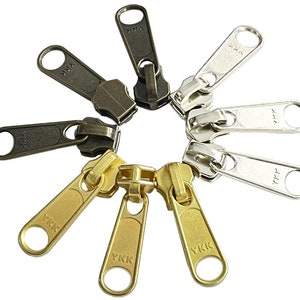 May include: A set of eight zipper pulls in various finishes, including antique brass, nickel, and gold. Each pull features the YKK logo.