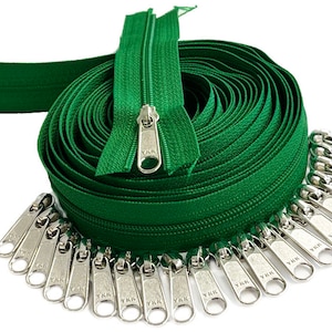 May include: A roll of green zipper tape with silver YKK zipper pulls. The tape is coiled and the pulls are arranged in a semi-circle.