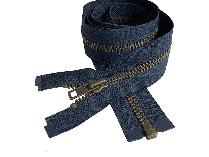May include: A navy blue zipper with brass teeth and a slider. The zipper is coiled and ready to be sewn into a garment.