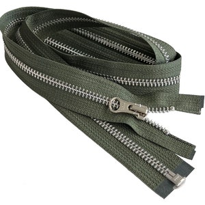 Puede incluir: Una cremallera verde con dientes plateados y un deslizador plateado. La cremallera está enrollada y lista para ser utilizada en proyectos de costura.