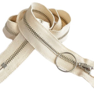 May include: A white cotton zipper with a silver metal slider and pull tab. The zipper is closed and has a herringbone pattern.