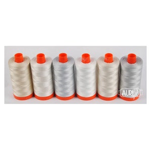 May include: Six spools of thread in various shades of white and gray. The spools are arranged in a row and have orange tops.