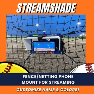 May include: A blue and white StreamShade phone mount for streaming, attached to a black fence. The phone displays a game. Text on the mount reads "Diamond Dogs". The image also includes the text "Fence/Netting Phone Mount for Streaming" and "Customize Name & Colors!"