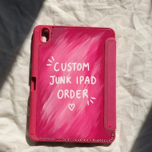 Puede incluir: Una funda para tableta de color rosa brillante con una textura de pinceladas pintadas a mano en varios tonos de rosa. El centro presenta texto blanco que dice CUSTOM JUNK IPAD ORDER con un pequeño corazón debajo. Estrás decora el borde inferior.