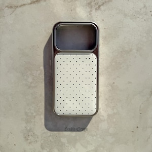 May include: A phone case with a white background and a pattern of small black dots. The case has a silver-colored frame and a camera cutout. The text "Studio Eleven" is printed at the bottom.