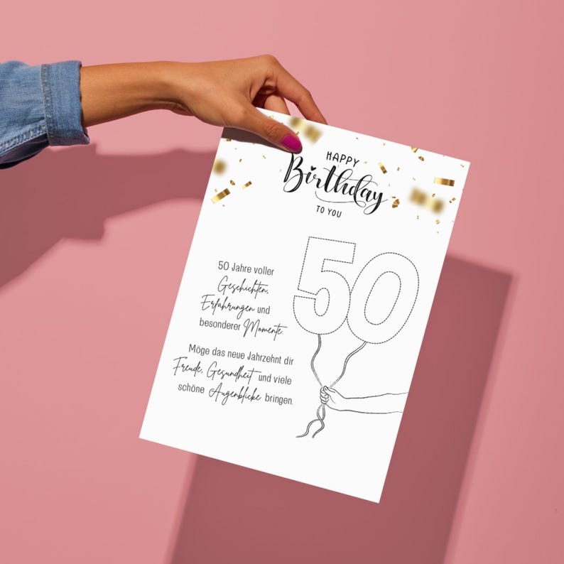 Puede incluir: Una tarjeta de cumplea&ntilde;os blanca con las palabras "Happy Birthday To You" en escritura elegante. El n&uacute;mero "50" est&aacute; dise&ntilde;ado como globos, sostenidos por una mano. Confeti dorado acent&uacute;a el dise&ntilde;o. La tarjeta se sostiene sobre un fondo rosa.