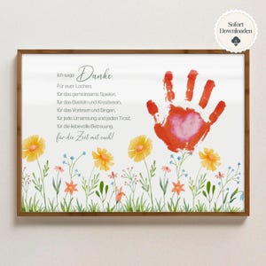 May include: A framed print with a watercolour design. The print features a red handprint with a heart, floral illustrations, and German text. The text includes the word "Danke" and other phrases.