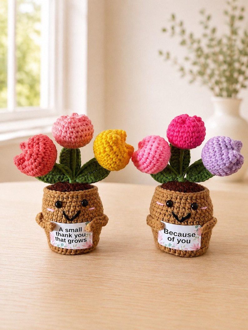 May include: Two crocheted potted plants with smiling faces, each holding a small sign. The left plant has pink, yellow, and red tulips with a sign reading A small thank you that grows. The right plant has pink and purple tulips with a sign reading Because of you.