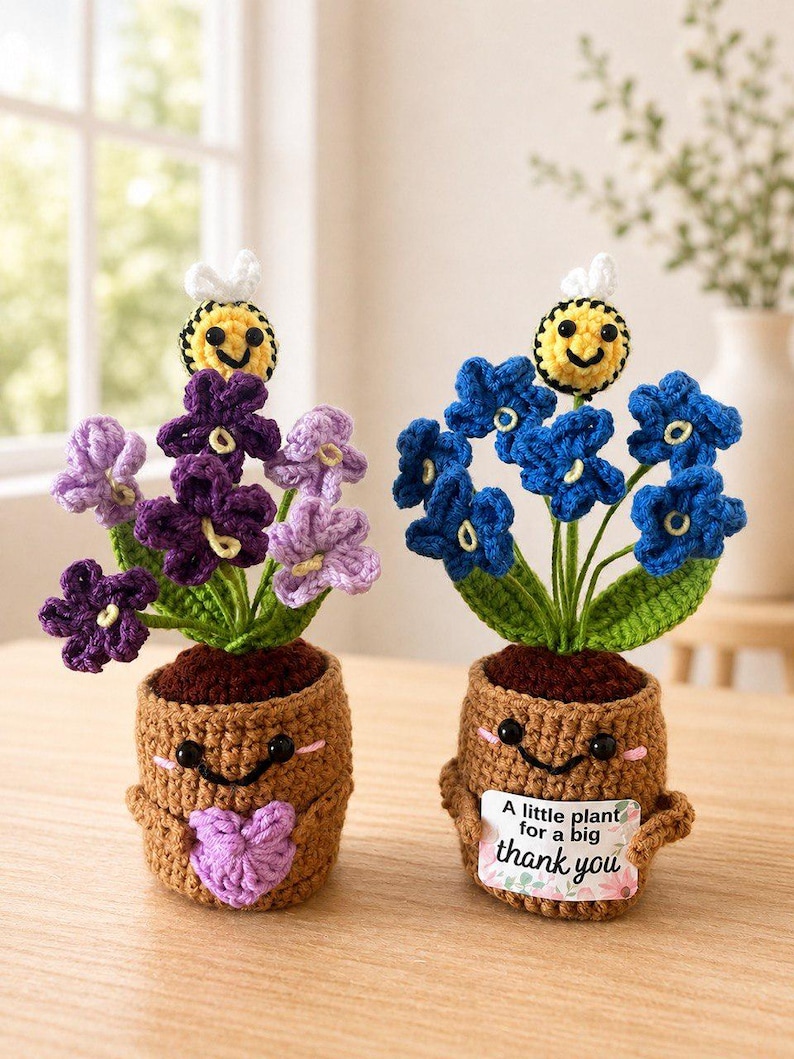 May include: Two crocheted potted plants with smiling faces. One has purple flowers and a purple heart, the other has blue flowers and a sign that reads A little plant for a big thank you. Both feature a small yellow and black bee on top.