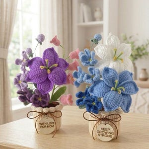 May include: Two crocheted flower arrangements in beige pots. The left pot has a tag reading WITH LOVE FOR MOM, featuring purple and pink flowers. The right pot has a tag reading KEEP GROWING STRONG, featuring blue and white flowers with green stems.
