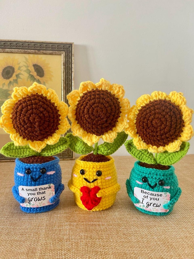 May include: Three crocheted sunflowers in pots. The blue pot holds a sign reading A small thank you that grows. The yellow pot features a red heart. The teal pot holds a sign reading Because of you I grew. Each pot has a smiling face.