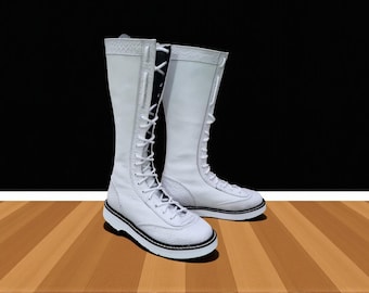 May include: A pair of white knee-high boots with a lace-up design and a textured pattern. The boots have a white sole with a black trim and are set against a black and brown background.