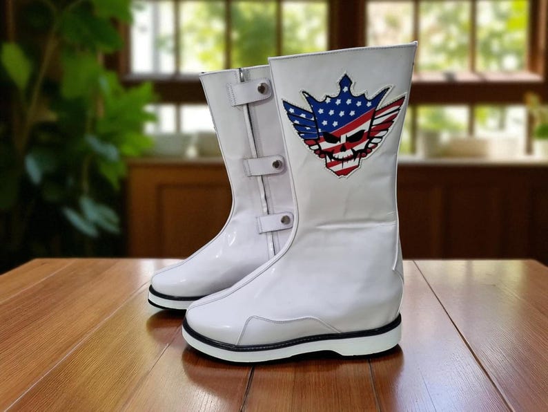 May include: Pair of white, high-top boots with a glossy finish. Each boot features a black sole and a decorative patch with a skull, crown, and American flag design. The boots have buckles and a zipper closure.