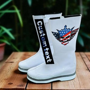 May include: A pair of white boots with a black and white sole. The boots have a graphic of a skull with a crown, wings, and an American flag design. The text "Custom text" is printed on a black strip.