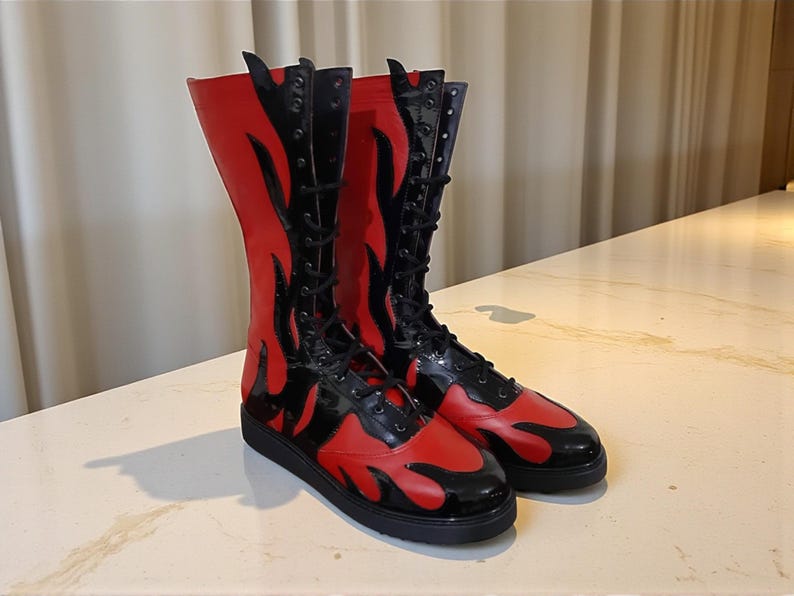 May include: A pair of knee-high boots with a striking flame design. The boots are primarily red with black accents, including the laces and the flame details. The boots have a flat sole and a glossy finish.