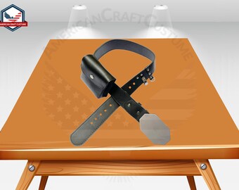 May include: A black leather belt with a buckle and a pouch. The belt is on a wooden table with a brown surface.