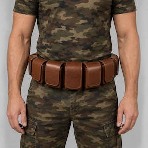 May include: A brown leather utility belt featuring multiple rectangular pouches attached around the waist. The belt is worn over a camouflage t-shirt and camouflage cargo trousers, showcasing a structured design with smooth, solid brown leather compartments.