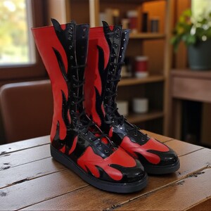 May include: A pair of tall, red and black boots with a flame design. The boots have a lace-up closure and a black sole. The boots are made of a shiny material and are displayed on a wooden surface.
