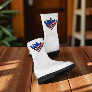 May include: A pair of white boots with a black sole, featuring a graphic of a skull with a blue and red American flag design. The boots are made of a glossy material and are displayed on a wooden surface.