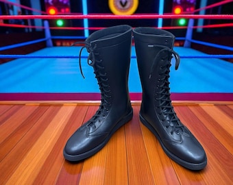 May include: A pair of black, knee-high boots with a lace-up design. The boots are made of a smooth material and have a flat sole. They are displayed on a wooden floor with a wrestling ring in the background.