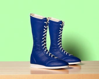 May include: A pair of blue high-top boots with white laces and soles. The boots are made of a smooth material and are set against a light green background. The boots are approximately 12 inches tall.
