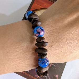 Op de afbeelding: Een armband met koffiebonen en blauwe en roze gemarmerde kralen. De armband is geregen, waardoor een uniek en natuurlijk accessoire ontstaat. Een uniek sieraad.