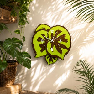 May include: A wall clock shaped like a cluster of three begonia leaves with bright lime green edges and dark brown centers. The clock face features white hour and minute hands, with the numbers 12, 3, 6, and 9 printed in white on the leaves.
