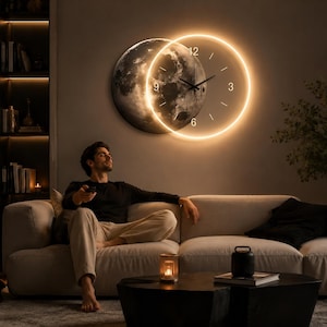 Può includere: Un orologio da parete circolare con una grafica dettagliata della superficie lunare, parzialmente illuminato da un anello LED a luce calda. Il quadrante presenta sottili lancette nere e indicatori orari minimalisti alle ore 3, 6, 9 e 12.