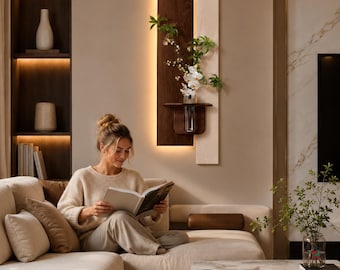 May include: A wall-mounted light fixture featuring a dark wood panel and a lighter wood panel, with a small shelf holding a clear glass vase containing white flowers and green foliage, illuminated by a warm LED light strip behind the dark panel.