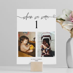 May include: A white card with the text "when we were 1" in black cursive script. The card has two photos of a baby, one in a bathtub and one in a stroller. The text "ALYSSA & ANDREW 9.28.24" is at the bottom of the card.