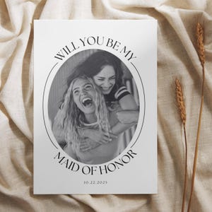 May include: A black and white photo of two women smiling and hugging. The text "Will you be my Maid of Honor? 10.22.2025" is printed below the photo.