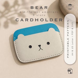 Puede incluir: Un tarjetero beige y azul con un diseño de cara de oso. El tarjetero tiene una parte superior azul y un cuerpo beige con ojos de puntos negros y una boca cosida. El texto "BEAR CARDHOLDER" está en la parte superior.