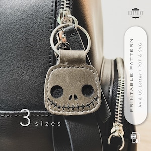 May include: A gray leather skull keychain with stitched details, attached to a silver keyring. The keychain is hanging on a black bag. The image also includes the text "3 sizes" and "Printable Pattern".