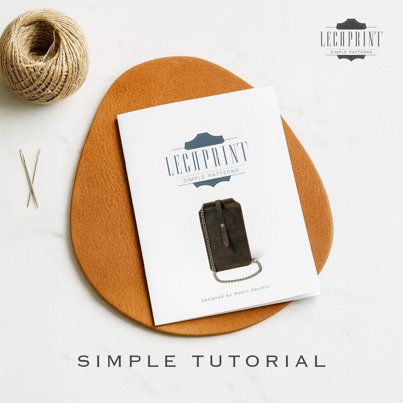 May include: A white booklet with the text "LECAPRINT SIMPLE PATTERNS" and an illustration of a dark brown leather wallet with a chain. The booklet is on a brown leather-like surface, with a ball of twine and needles.
