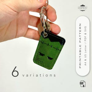 May include: Green leather keychain with a Frankenstein's monster face design. The keychain has a black top and stitched details, with a silver keyring and key attachments. The image also includes the text "6 variations".