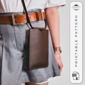 Könnte beinhalten: Ein braunes Leder-Handy-Etui mit einem Riemen, der an einem braunen Ledergürtel befestigt ist. Das Etui hängt am Gürtel und wird von einer Person getragen. Der Text "PRINTABLE PATTERN" ist auf dem Bild zu sehen.