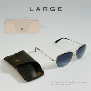 K&ouml;nnte beinhalten: Ein braunes Leder-Brillenetui mit Klappenverschluss. Das Etui ist 16 cm breit und 7 cm hoch. Das Etui ist neben einer Sonnenbrille mit goldfarbenem Gestell und dunklen Gl&auml;sern abgebildet.