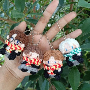 以下が含まれることがあります： 手作りの編みぐるみキャラクターキーホルダー4個セット。各キーホルダーは、糸の髪、スカーフ、服を着た小さな人形のようなフィギュアが特徴です。キーホルダーはシルバーカラーのボールチェーンに取り付けられています。フィギュアは、茶色、黒、グレー、赤など、さまざまな色です。